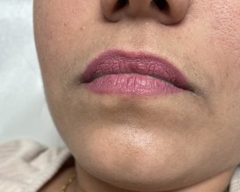 Close-up of a person’s lower face and lips wearing pink lipstick, with visible skin texture and light facial hair.