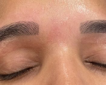 A close-up of closed eyes showing freshly microbladed eyebrows on smooth skin.