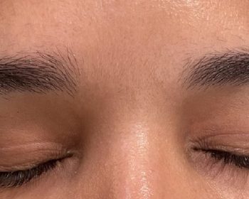 A close-up of a person’s closed eyes and eyebrows with natural, untrimmed hair growth.